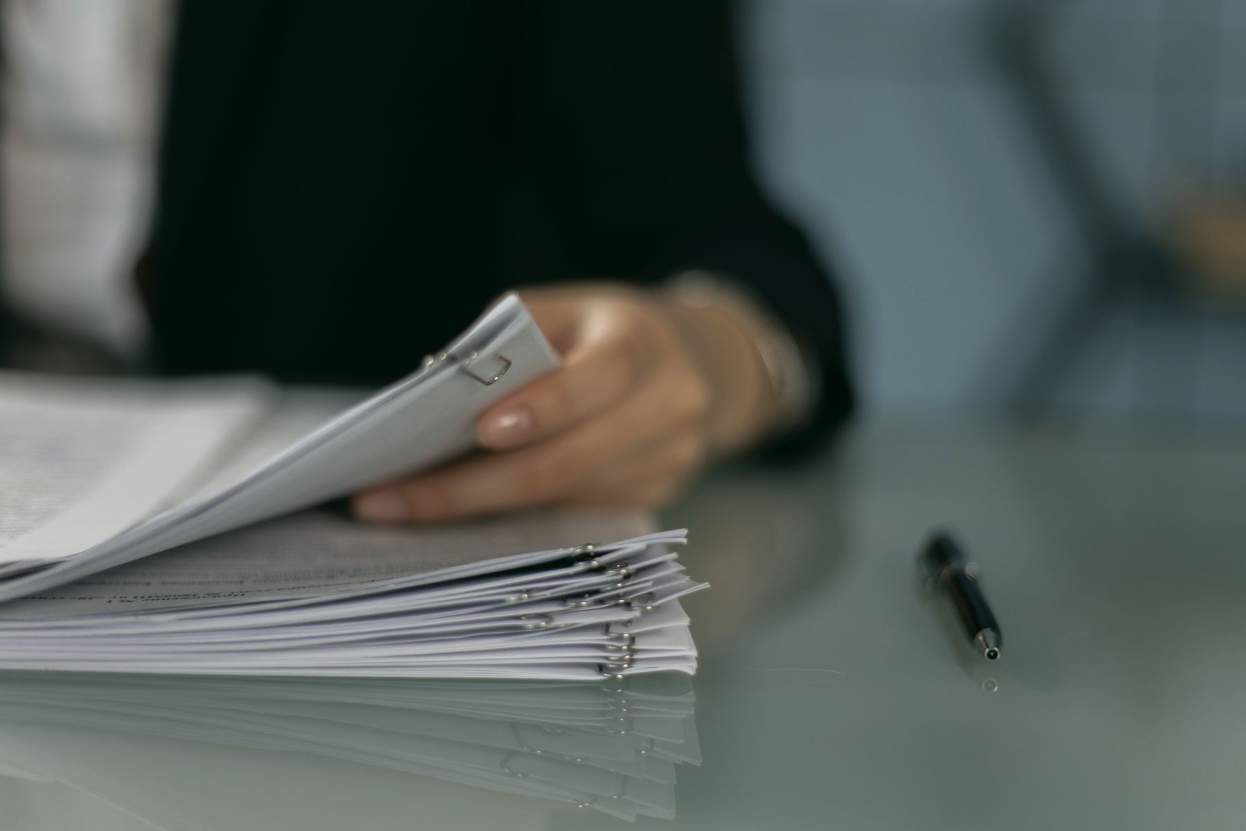 A hand resting on a stack of clipped papers, with a pen beside it.